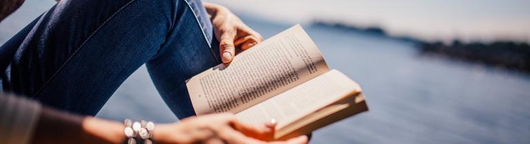 Mann sitzt am See und liest ein Buch