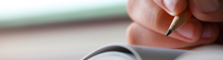 Hand schreibt mit Bleistift in ein Heft