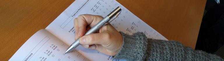 Hand füllt mit Kugelschreiber ein Mathe Dossier aus