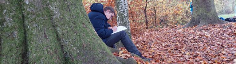Student sitzt im Wald und schreibt etwas auf