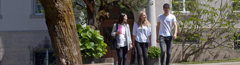 Drei Studenten gehen einen Weg lang weg von einem Gebäude