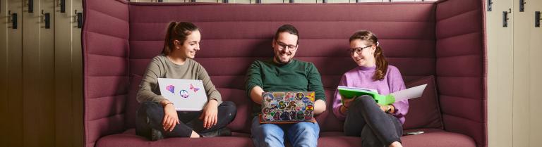 3 Studierende sitzen auf dem Sofa und schauen in einen Laptop
