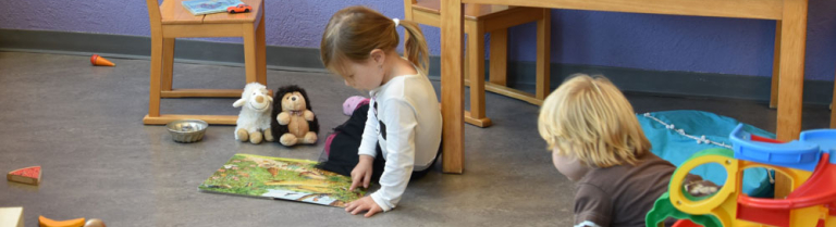 Mädchen betrachtet am Boden sitzend Bilderbuch mit Plüschtieren