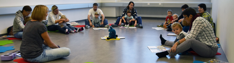 Erwachsene und Kinder sitzen in einer Gruppe am Boden