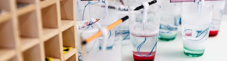 Diverse Proben mit farbiger Flüssigkeit stehen in Gläsern auf dem Labortisich