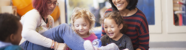 Zwei erwachsene Frauen sitzen mit zwei Kindern spielend am Boden