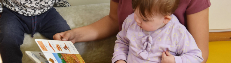 Fachperson betrachtet Bilderbuch mit zwei kleinen Kindern