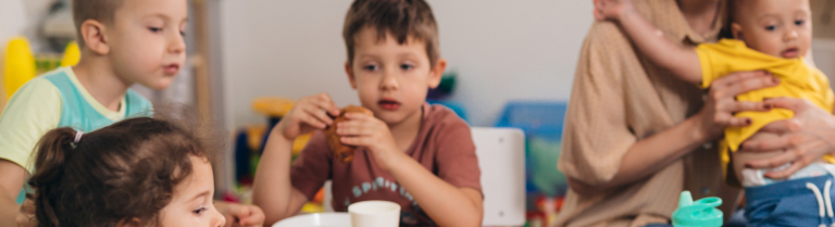 Kinder sitzen zum essen mit Betreuerinnen an einem Tisch 