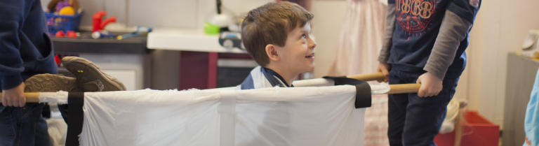 Zwei Kinder tragen ein Kind in einer Trage