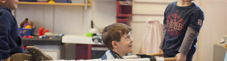 Zwei Kinder tragen ein Kind in einer Trage