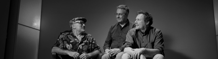 Drei Personen sitzen auf einer Bühne.