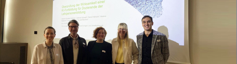 Fünf Personen stehen vor einer Präsentationsfolie zu einer Tagung