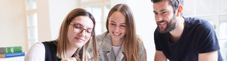 Drei Student:innen schauen auf ein Tablet
