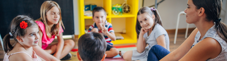 Erwachsene Person sitzt mit Kindern in einem Kreis am Boden