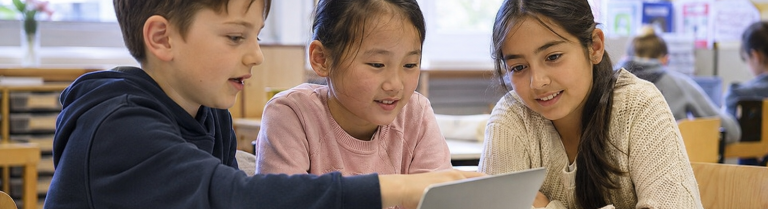Drei Primarschulkinder arbeiten gemeinsam an einem Laptop im Klassenzimmer