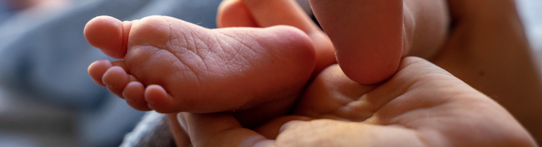 Hände einer erwachsenen Person halten zwei Kleinkinderfüsschen