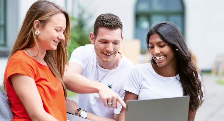 3 Studierende schauen in einen Laptop