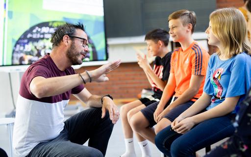 Lehrer erklärt 3 Mittelstufenschülern etwas mit einer Handgeste