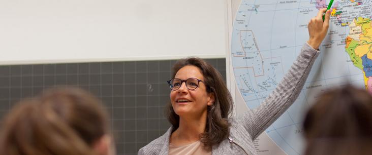 Lehrerin zeigt Lernenden ein Land auf einer Weltkarte