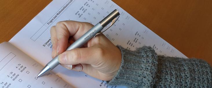Hand füllt mit Kugelschreiber ein Mathe Dossier aus