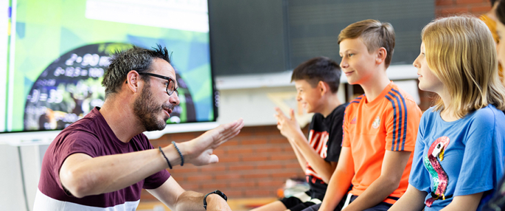 Lehrer erklärt 3 Mittelstufenschülern etwas mit einer Handgeste