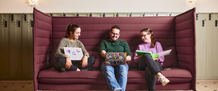 3 Studierende sitzen auf dem Sofa und schauen in einen Laptop