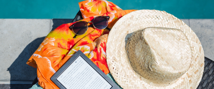 Ein Strandtuch, ein E-Reader, eine Sonnenbrille und ein Strohhut liegen neben einem Pool.