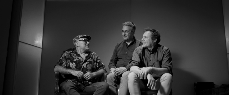 Drei Personen sitzen auf einer Bühne.