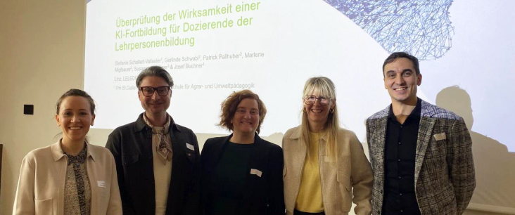 Fünf Personen stehen vor einer Präsentationsfolie zu einer Tagung