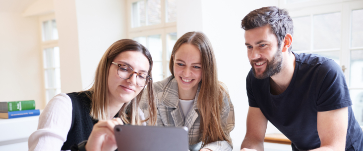 Drei Student:innen schauen auf ein Tablet