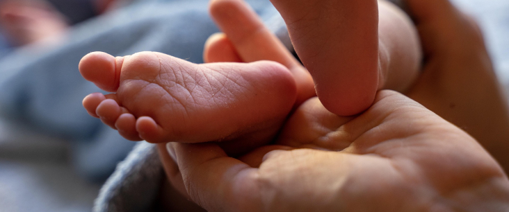 Hände einer erwachsenen Person halten zwei Kleinkinderfüsschen