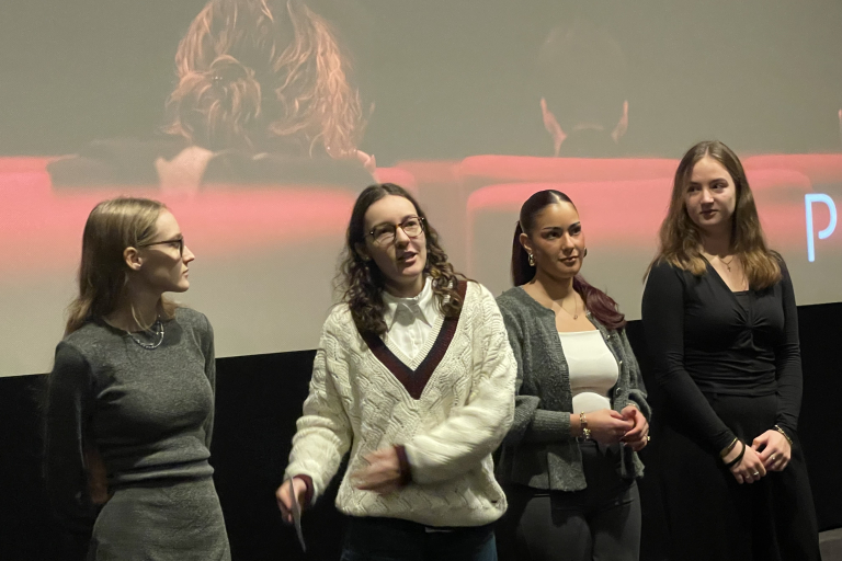 Vier Personen stehen auf der Kinobühne vor der Leinwand