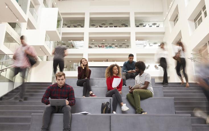 Personen sitzen in einem Campus mit Laptops auf einer Treppe