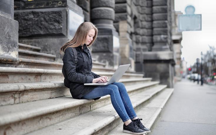 Schülerin sitzt vor der Schule mit Laptop 