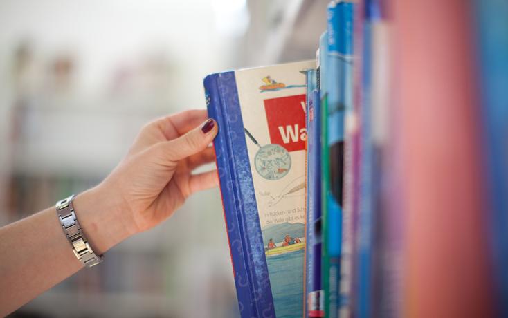 Hand greift Buch aus Bibliotheksgestell