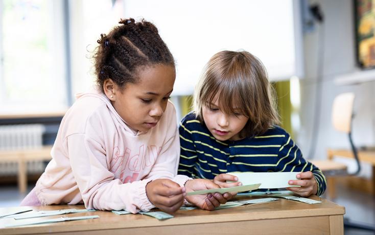 Zwei Grundschulkinder betrachten zusammen einen Zettel