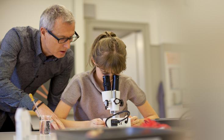 Lehrer begleitet Schülerin beim Gebrauch eines Mikroskop