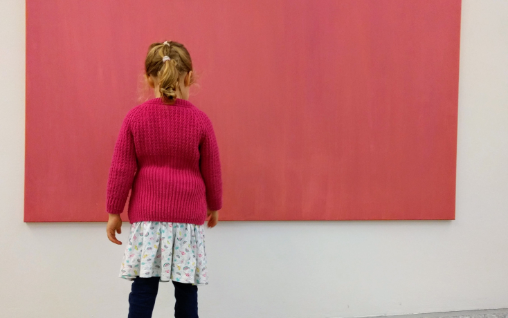 Ein kleines Mädchen mit pinkem Pullover steht vor einem pinken Bild