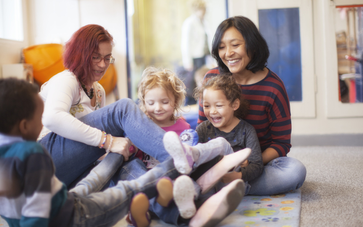 Zwei erwachsene Frauen sitzen mit zwei Kindern spielend am Boden