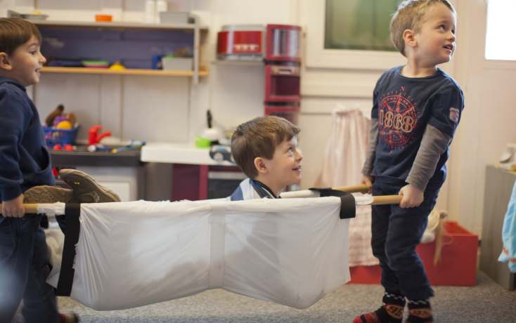 Zwei Kinder tragen ein Kind in einer Trage