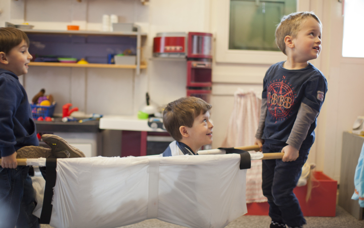 Zwei Kinder tragen ein Kind in einer Trage