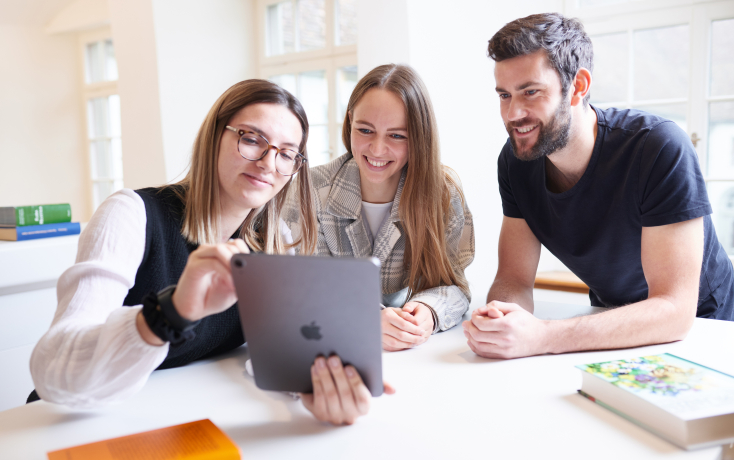 Drei Student:innen schauen auf ein Tablet