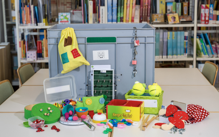 Graue Box mit vielen Spielsachen davor. 