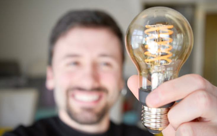 Mann hält leuchtende Glühbirne als Symbol für Inspiration und gewinnbringenden KI-Einsatz in der Hochschullehre