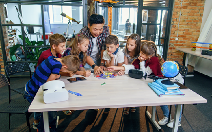 Lehrperson und Schulkinder arbeiten gemeinsam an einem Tisch in einem modernen Klassenzimmer mit digitalen Lernmitteln