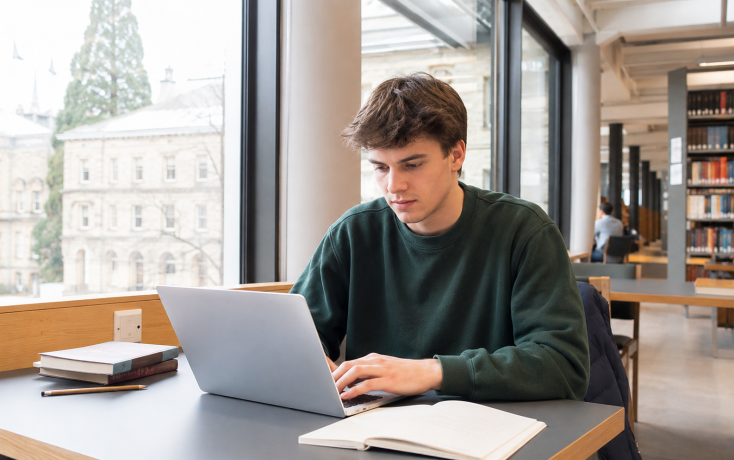 Studierender arbeitet konzentriert mit Laptop in einer Bibliothek als Symbol für digitale Basiskompetenzen