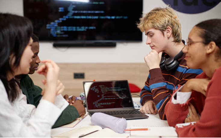 Gruppe Studierender diskutiert konzentriert vor einem Laptop mit Code auf dem Bildschirm