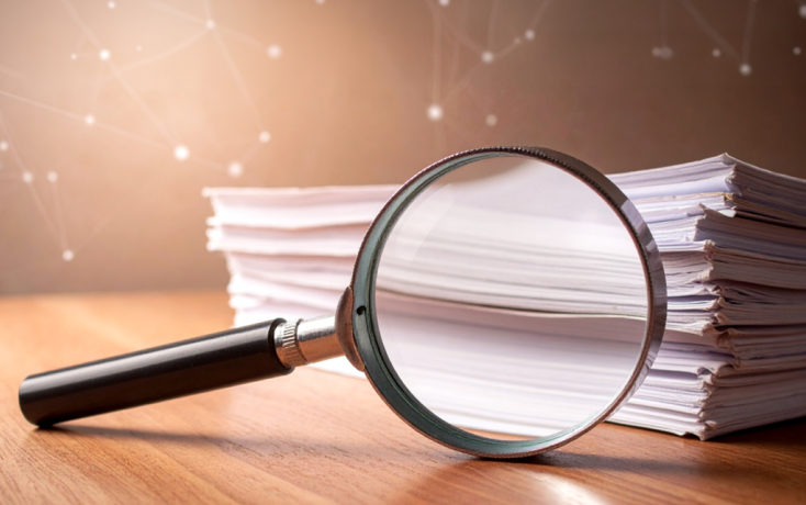 Lupe und Dokumentenstapel als Symbol für KI-Forschung, Publikationen, Referate und Expertise des IDIB