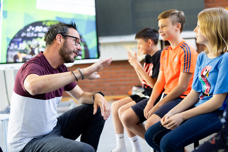 Lehrer erklärt 3 Mittelstufenschülern etwas mit einer Handgeste