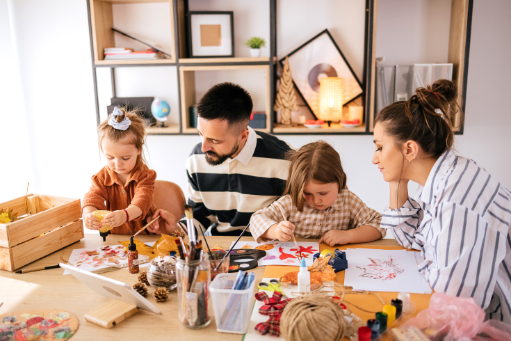 Zwei Erwachsene malen mit zwei Kindern an einem Tisch